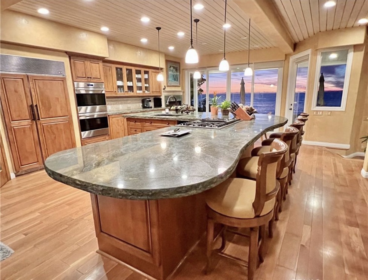 Completed kitchen remodel with warm wood cabinetry, curved stone island, and ocean view