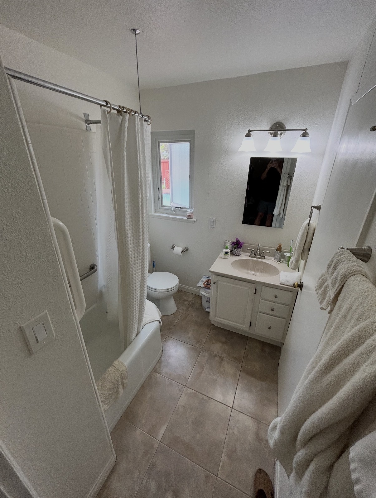 Bathroom before renovation with a bathtub-shower combo, off-white vanity, and tan tile floor