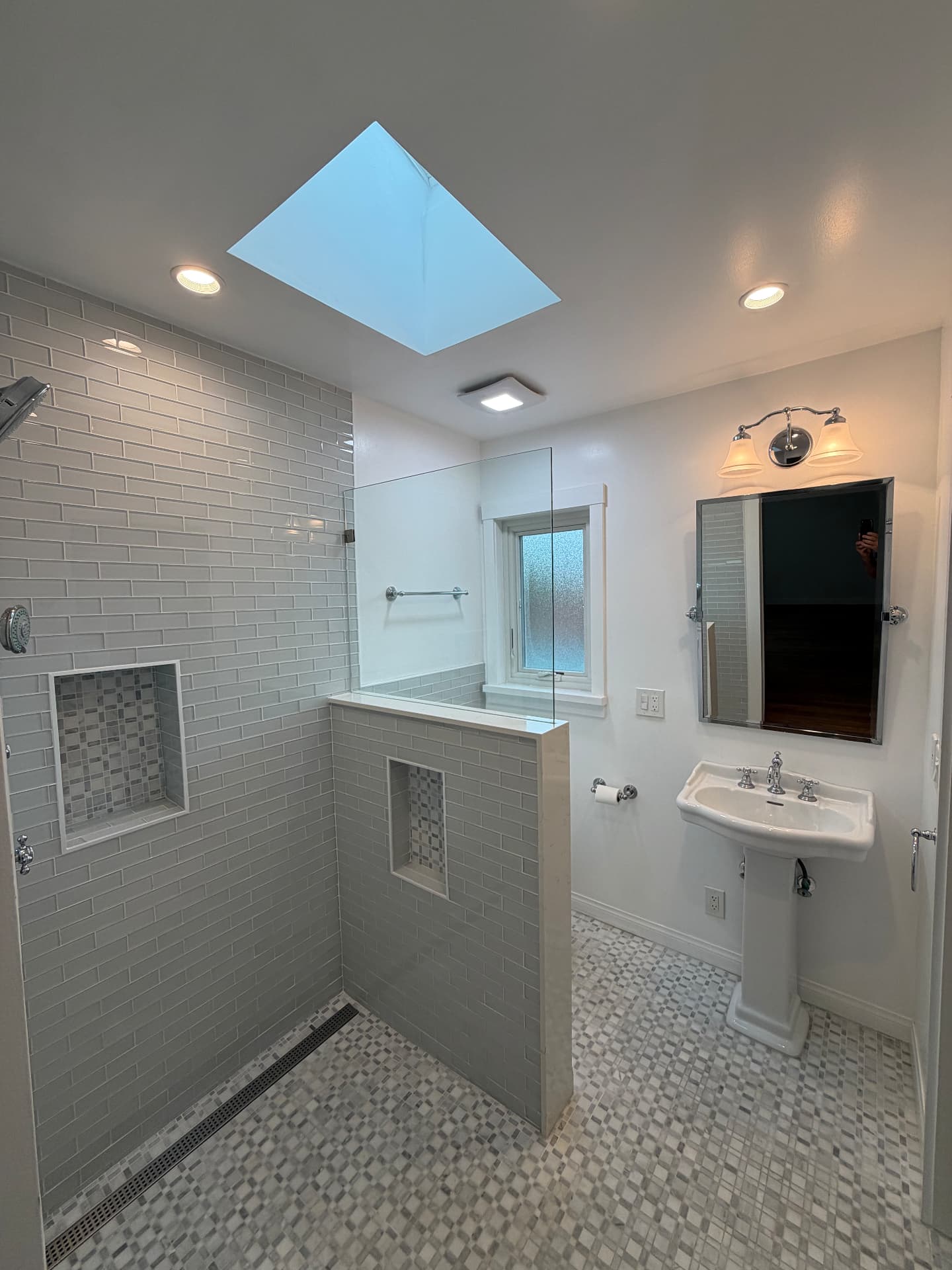 Remodeled bathroom with a curbless walk-in shower, gray subway tile, marble mosaic floor, and skylight