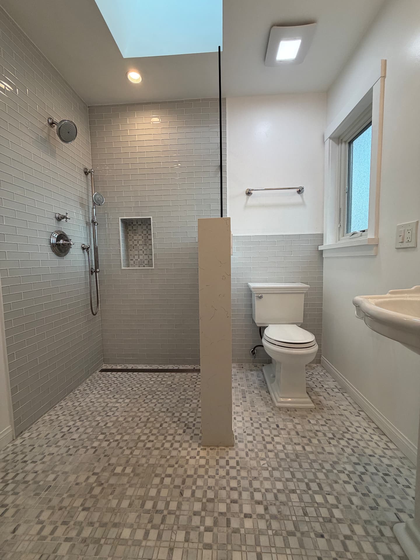 Remodeled bathroom with marble mosaic floor, gray subway tile wainscot, and a stone-capped partition wall