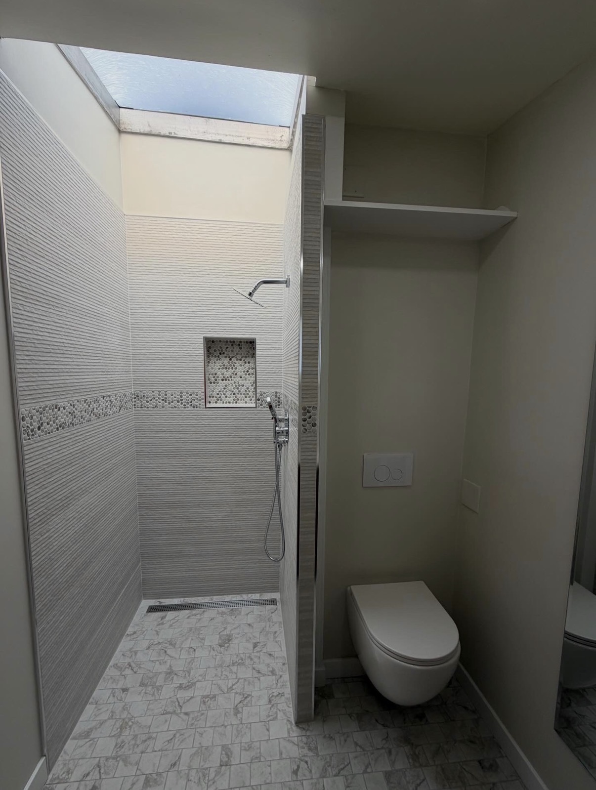 Completed bathroom remodel with skylit walk-in shower, textured tile, and wall-mounted toilet