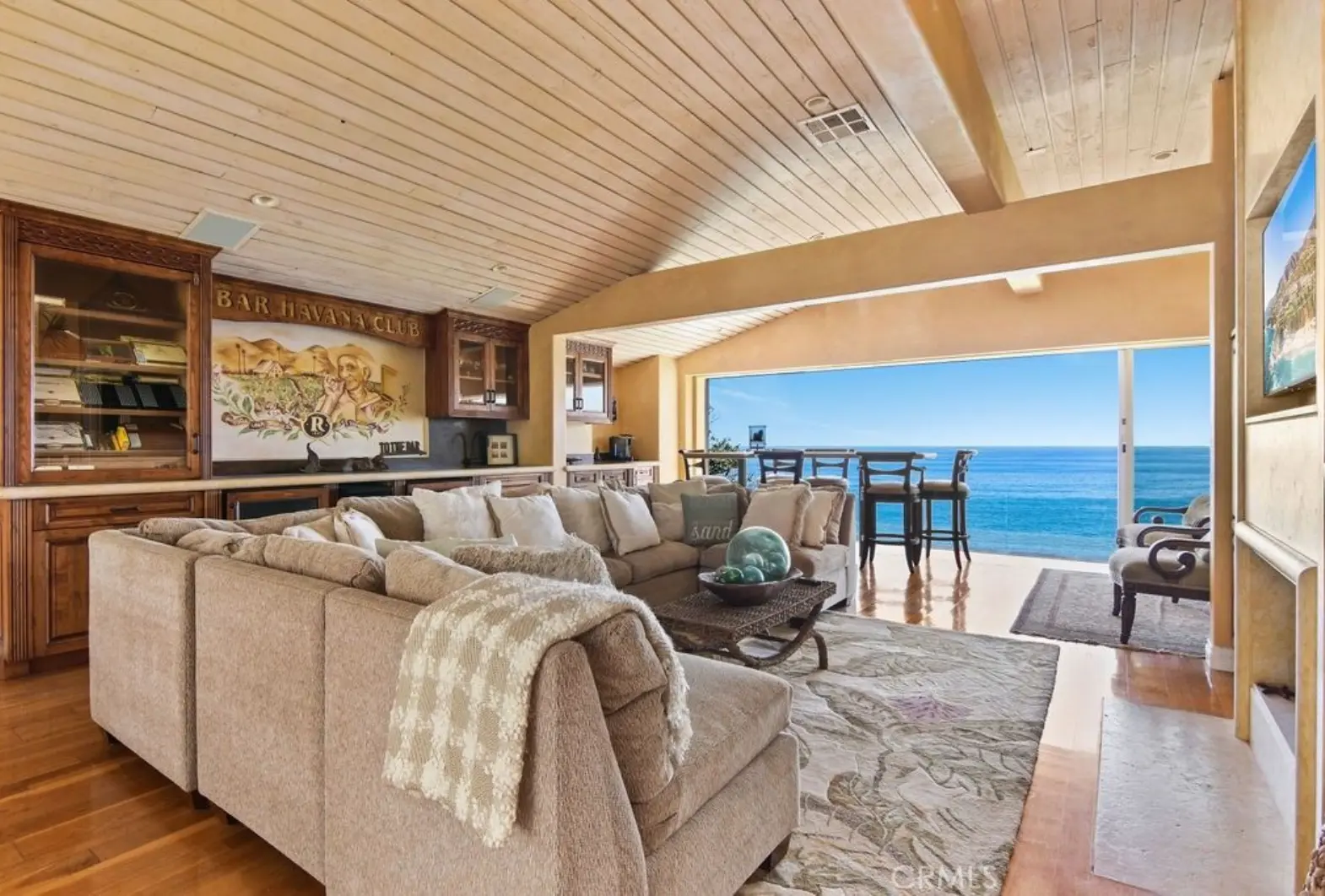 Coastal living room with custom bar cabinetry, vaulted wood ceiling, and ocean-view patio
