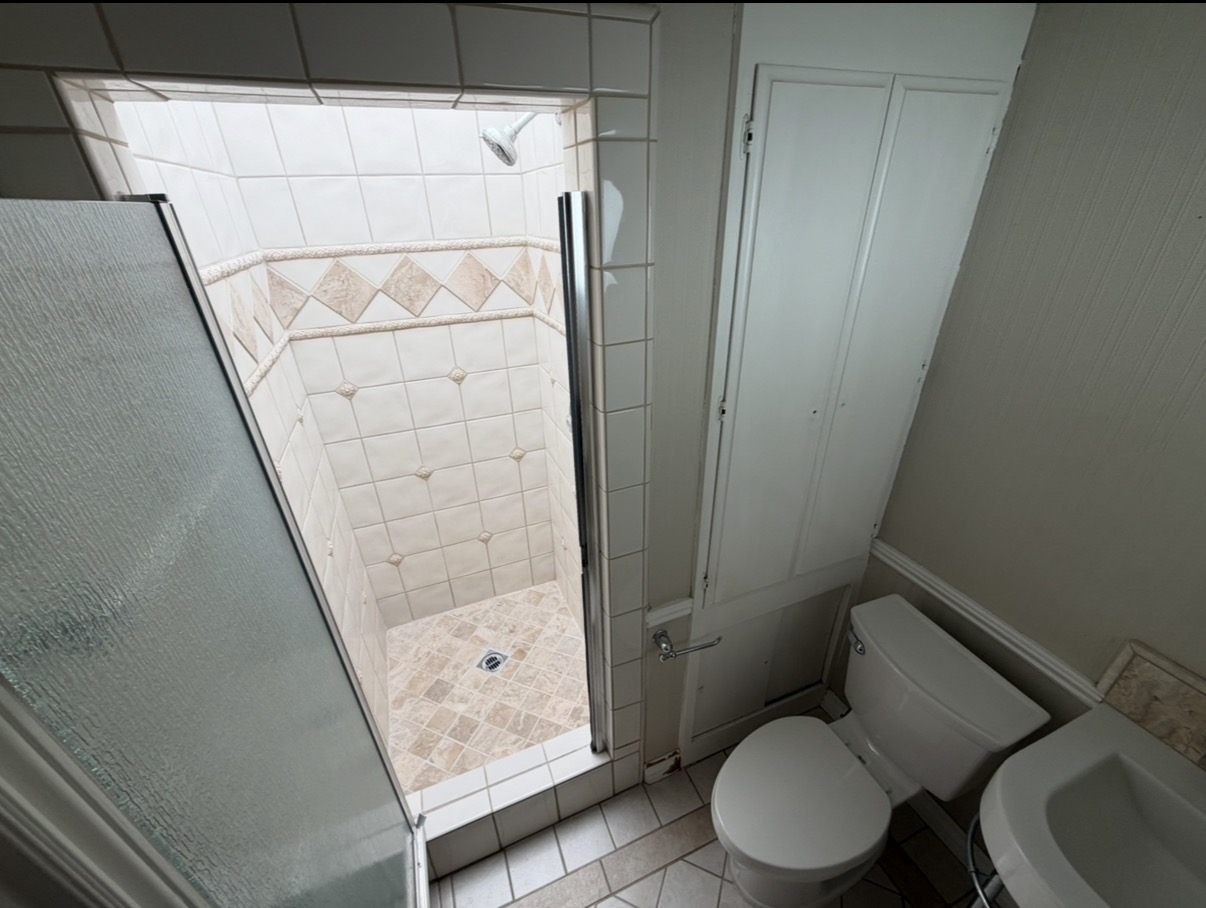 Bathroom before renovation with older tiled shower and frosted glass enclosure