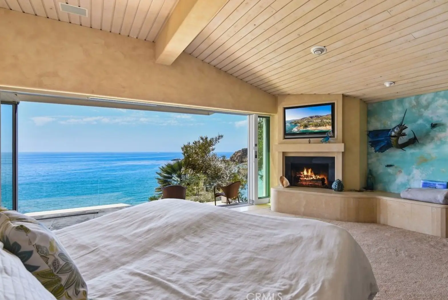 Primary bedroom with vaulted wood ceiling, fireplace, and wall of glass facing the ocean