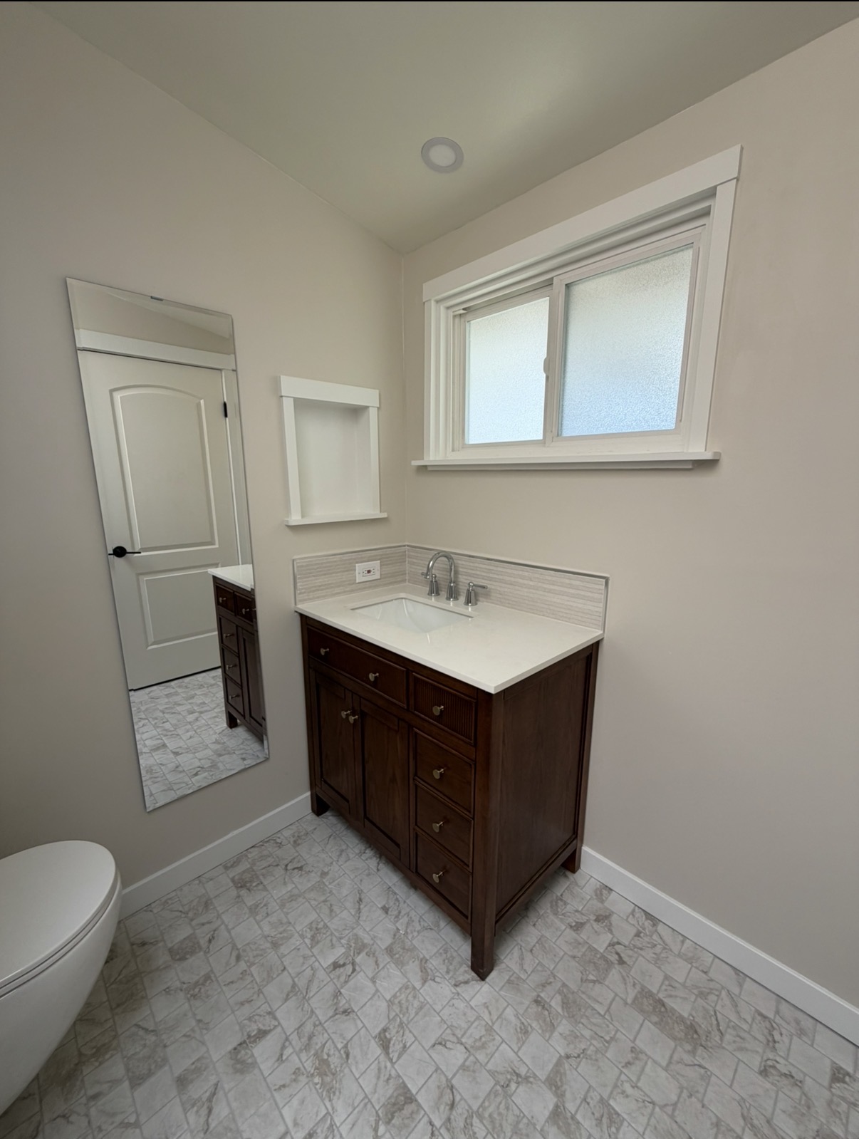 Finished bathroom vanity with walnut cabinet, quartz top, marble tile flooring, and built-in shelving niche